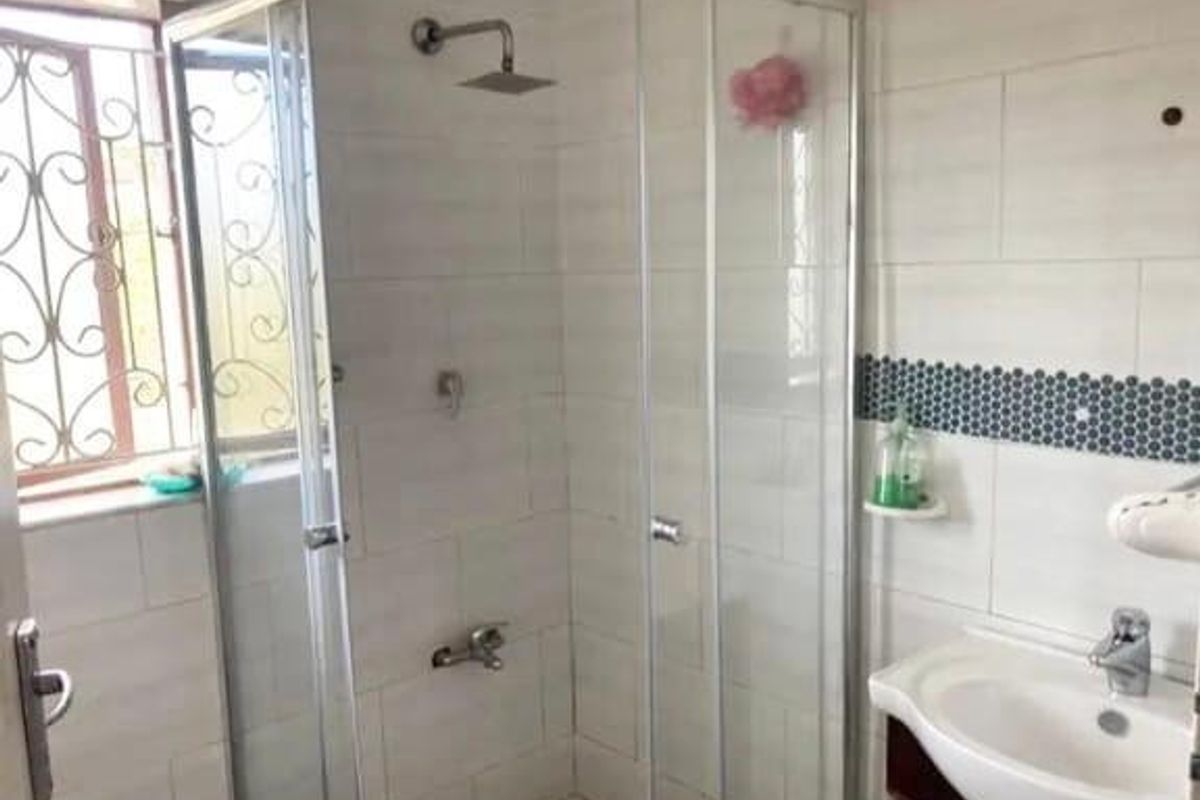 A functional bathroom featuring a glass-enclosed shower with a rain shower head, a vanity basin, and decorative mosaic wall tiling.