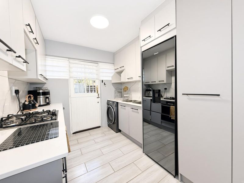 Modern kitchen featuring sleek cabinetry, gas cooktop, integrated appliances, and tiled flooring with direct access to the exterior.