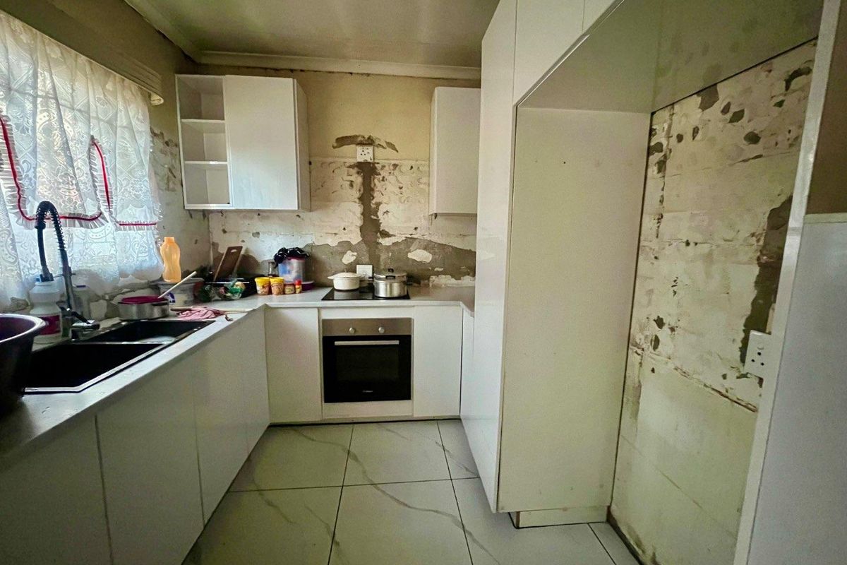 A kitchen featuring white cabinetry, built-in oven, and hob, currently requiring significant wall repairs and finishing to restore the space.