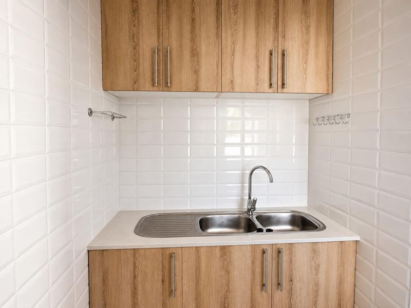 A clean and modern laundry area featuring wood-look cabinetry, a stainless steel double sink, and white subway tile splashbacks.