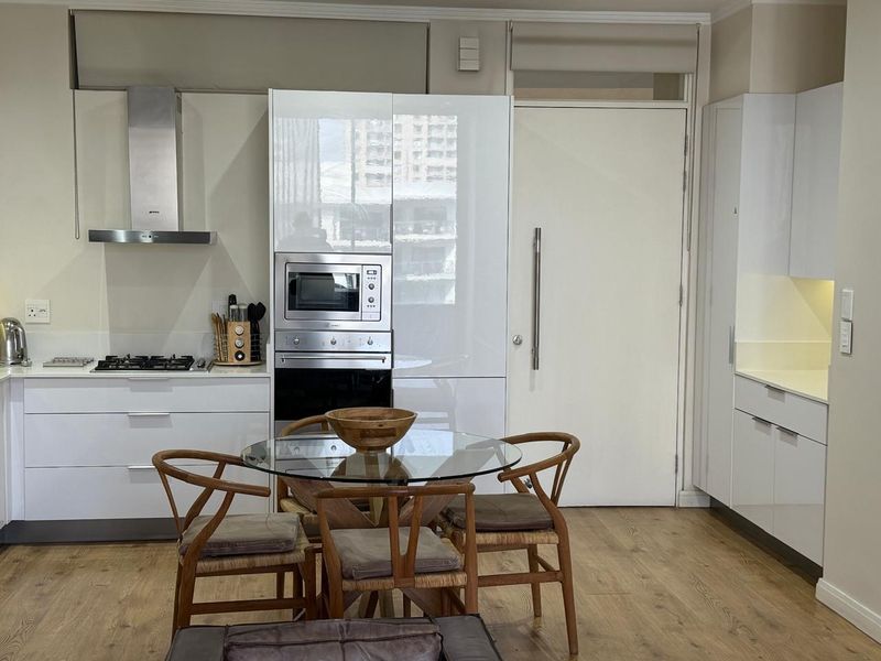 Modern open-plan kitchen featuring high-gloss white cabinetry, integrated stainless steel appliances, stone countertops, and durable laminate flooring.