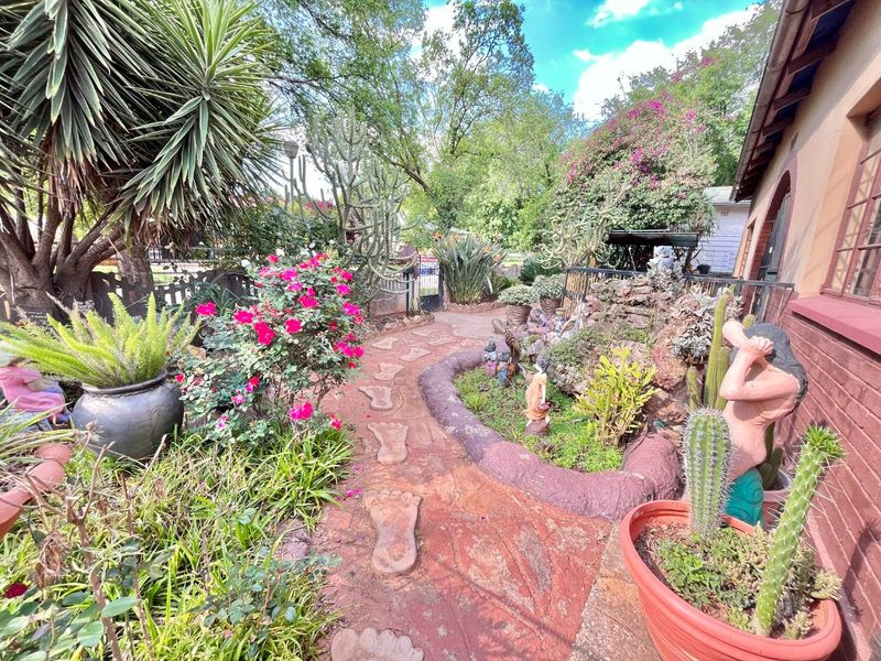 A lush, landscaped garden featuring a stone pathway, mature plantings, and brick exterior wall detailing.