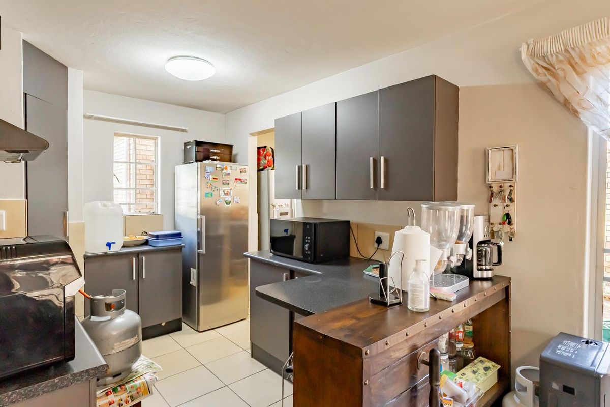 A functional kitchen featuring dark grey cabinetry, laminate countertops, tiled flooring, and an extractor fan, with direct access to an outdoor area.