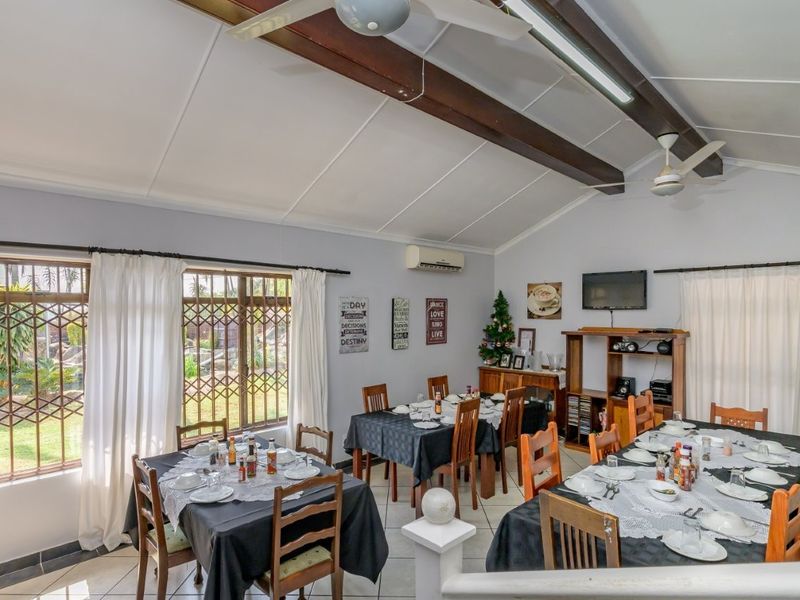Spacious dining area featuring exposed timber ceiling beams, tiled flooring, and large windows with security bars, offering a bright and functional space for gatherings.