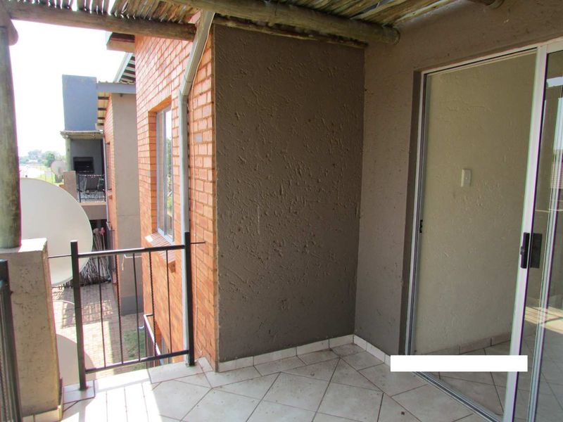 A covered balcony featuring tiled flooring, a metal balustrade, and a thatched roof structure, providing an outdoor space accessible via a sliding glass door.