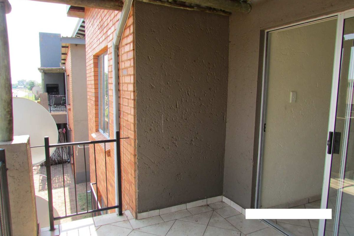 A covered balcony featuring tiled flooring, a metal balustrade, and a thatched roof structure, providing an outdoor space accessible via a sliding glass door.
