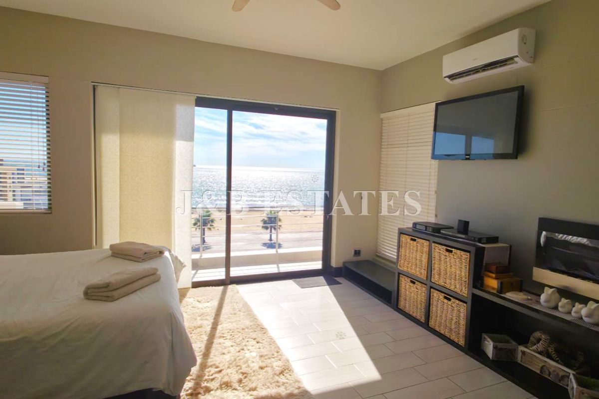 A bright bedroom featuring tiled flooring, a wall-mounted air conditioning unit, and sliding glass doors that open onto a balcony with ocean views.