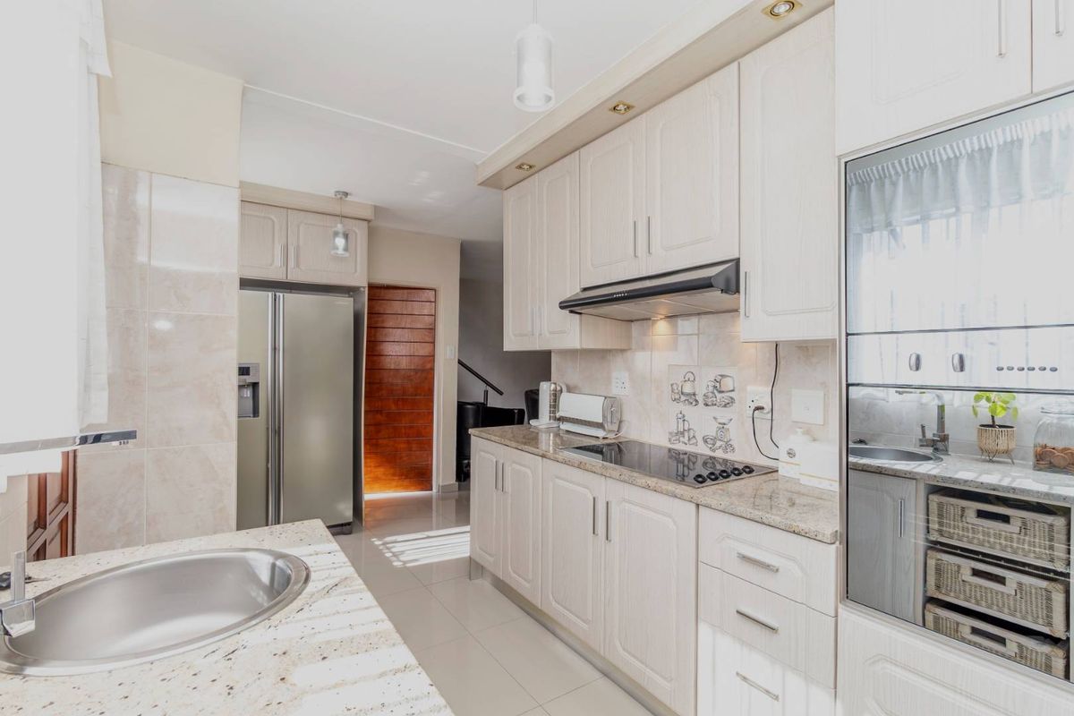 A well-maintained kitchen featuring granite countertops, built-in cabinetry, an electric hob with extractor fan, and tiled flooring.