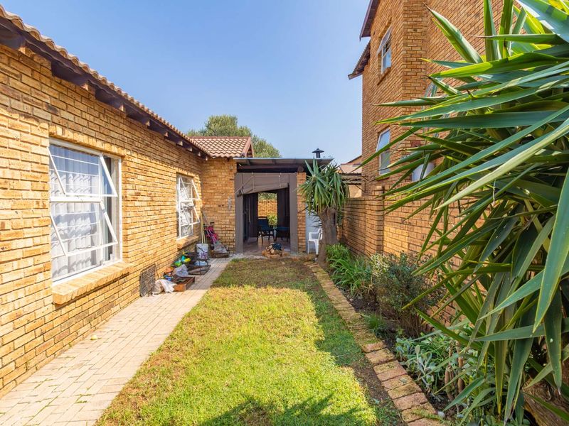 A rear exterior view of the townhouse featuring face brick walls, a paved walkway, a small lawn, and a covered patio area.