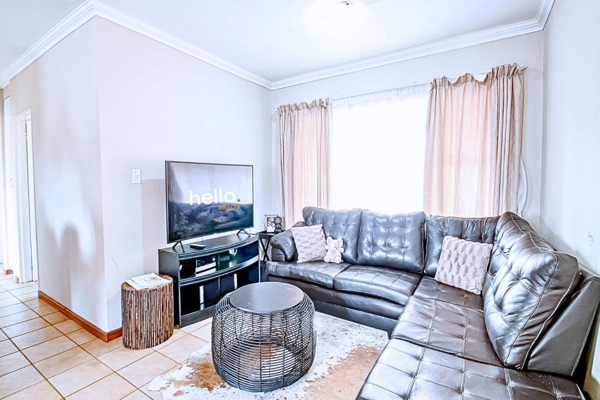 A bright living room featuring tiled flooring, crown molding, and a large window, providing a comfortable and functional space for relaxation.