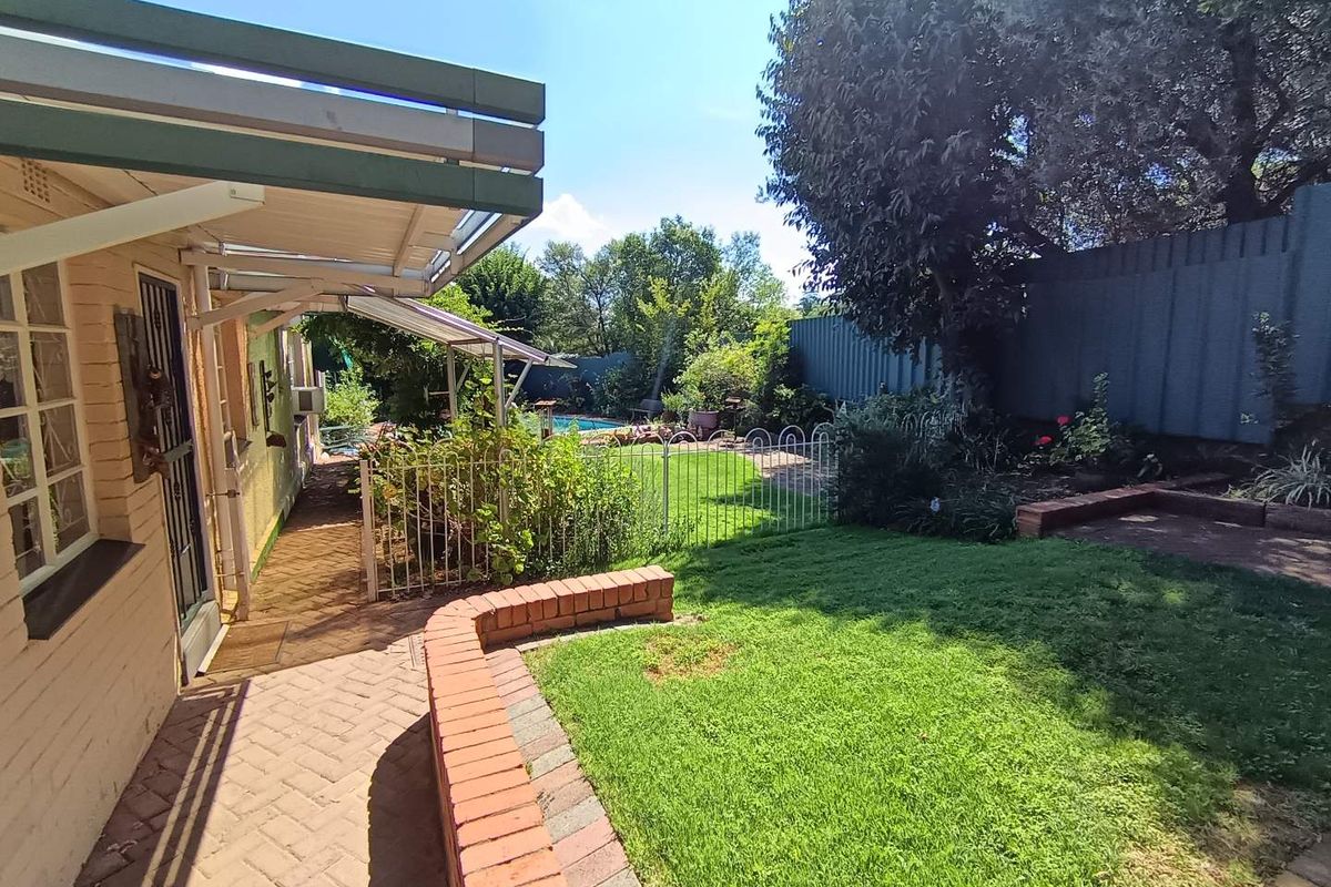 A rear garden area featuring a paved walkway, a brick retaining wall, a small lawn, and a covered patio section adjacent to the house.