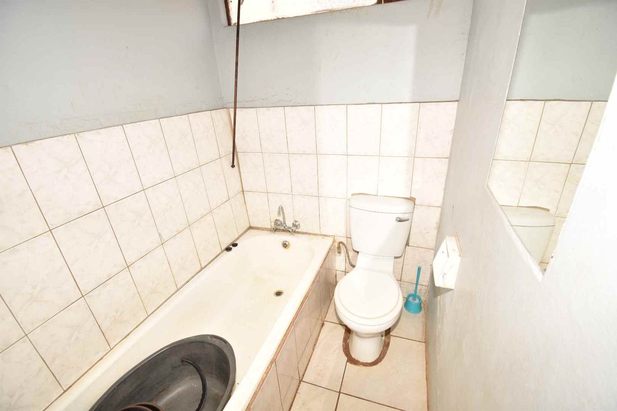 A compact bathroom featuring a standard bathtub, toilet, and wall-mounted mirror, requiring significant cosmetic updates and maintenance to improve its overall condition.