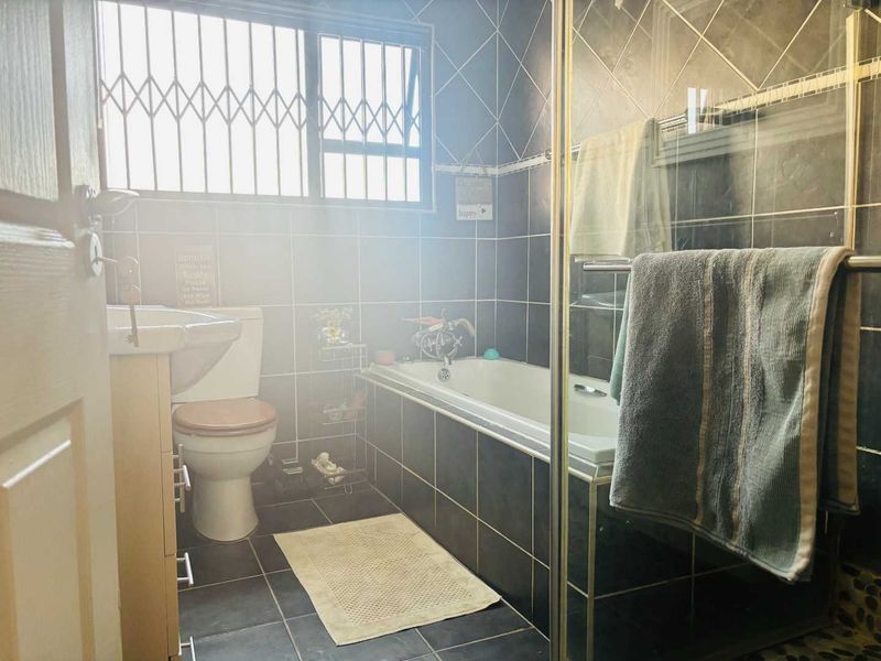 A functional bathroom featuring a bathtub, separate shower enclosure, pedestal basin, and toilet, finished with dark wall and floor tiling.