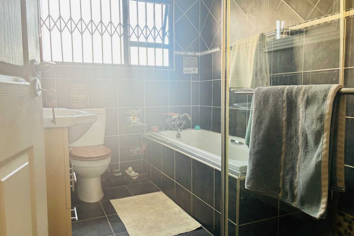 A functional bathroom featuring a bathtub, separate shower enclosure, pedestal basin, and toilet, finished with dark wall and floor tiling.