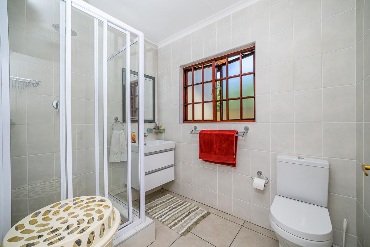 A clean and functional bathroom featuring a glass-enclosed shower, wall-mounted vanity, and a window with timber frames.