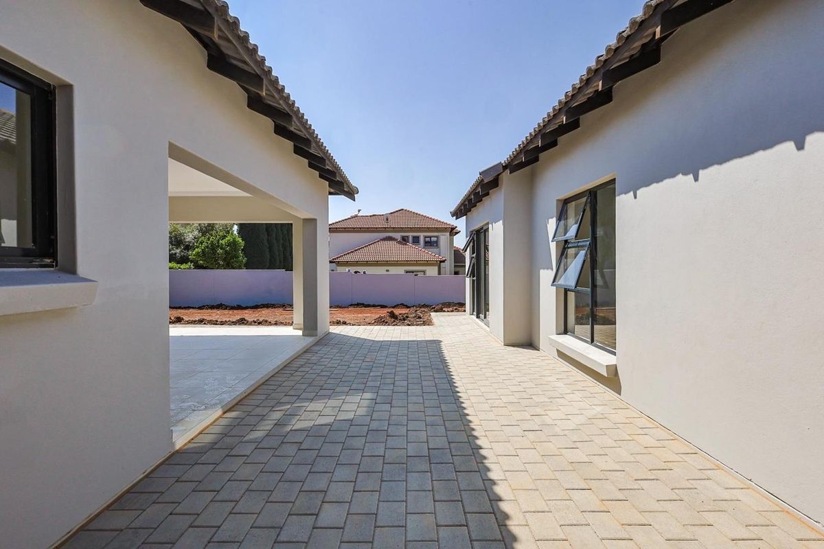 A paved outdoor courtyard area situated between two sections of the house, featuring modern tiled flooring and clean exterior wall finishes.
