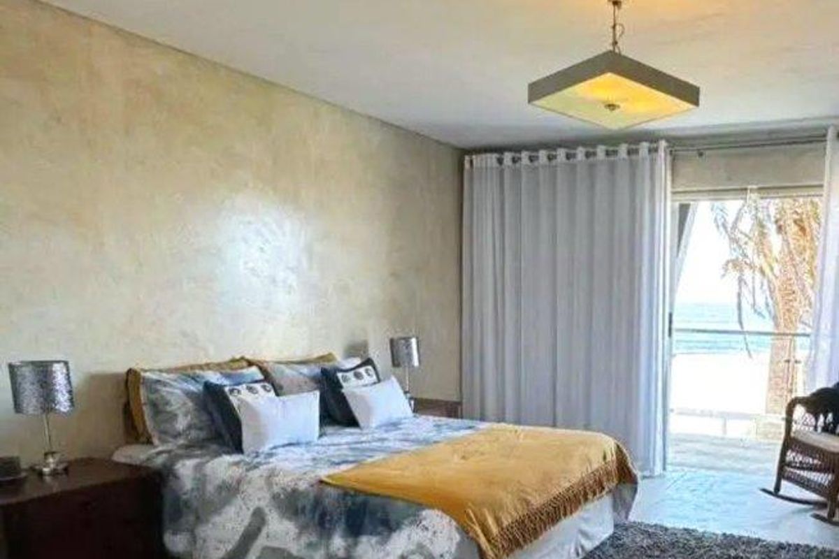 Spacious bedroom featuring textured feature wall, polished concrete flooring, and sliding glass doors opening to a private balcony with ocean views.