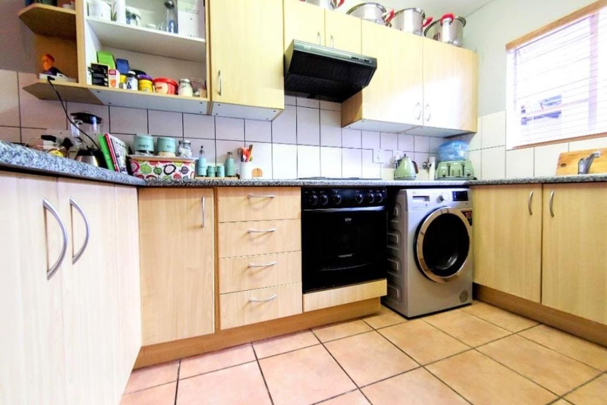 A functional kitchen featuring light wood-tone cabinetry, granite-look countertops, tiled backsplash, built-in oven with extractor fan, and space for a washing machine.