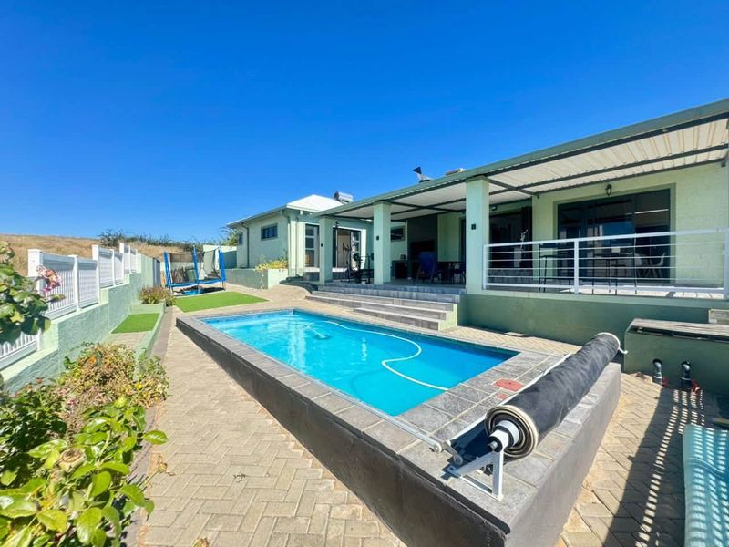 A well-maintained outdoor pool area featuring a paved patio, covered veranda, and secure perimeter fencing, ideal for outdoor relaxation and entertainment.