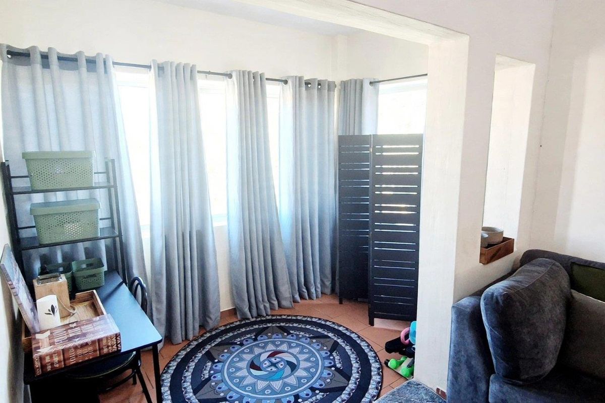 A bright living area featuring tiled flooring and large windows, providing ample natural light and a versatile space for relaxation or a home office setup.