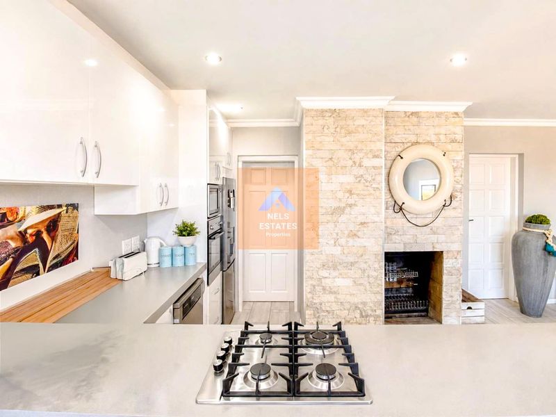 Modern kitchen featuring a central gas hob, built-in appliances, and a striking stone-clad fireplace feature wall, creating a warm and functional culinary space.