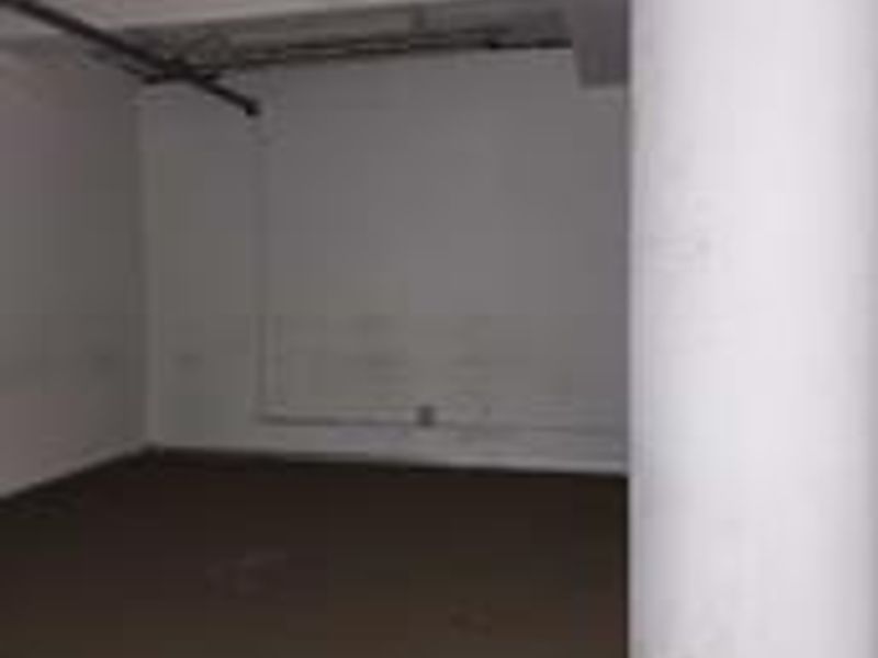 An empty, utilitarian commercial space featuring exposed ceiling infrastructure, a structural column, and basic wall finishes.