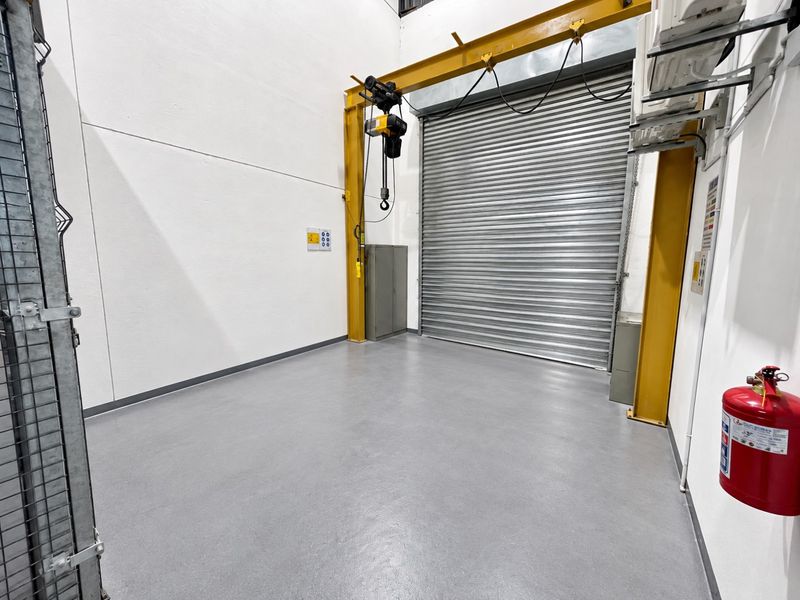 A clean, industrial-style garage space featuring a high-clearance roller shutter door, overhead crane, and durable epoxy flooring, suitable for storage or workshop use.
