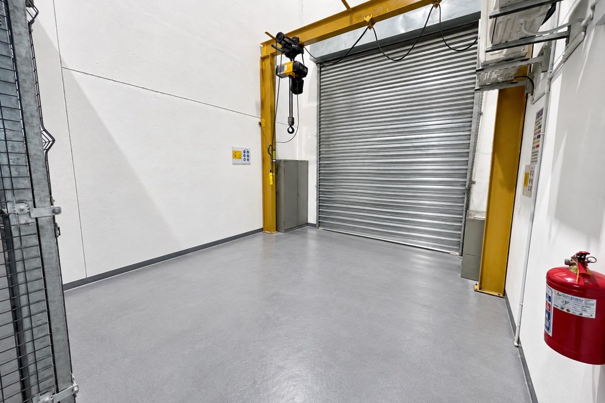 A clean, industrial-style garage space featuring a high-clearance roller shutter door, overhead crane, and durable epoxy flooring, suitable for storage or workshop use.
