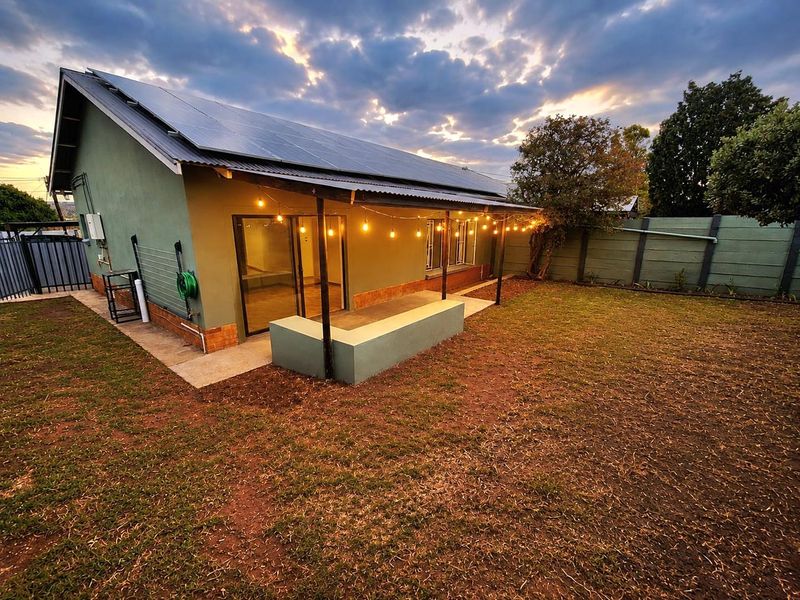 Rear view of the house featuring a covered patio with a built-in concrete bench, solar panels on the roof, and a private garden area.