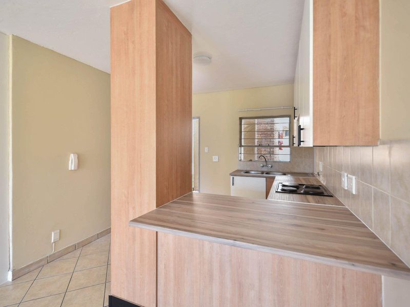 A functional kitchen featuring light wood-look cabinetry, laminate countertops, a built-in hob, and tiled flooring, offering a clean and practical workspace.