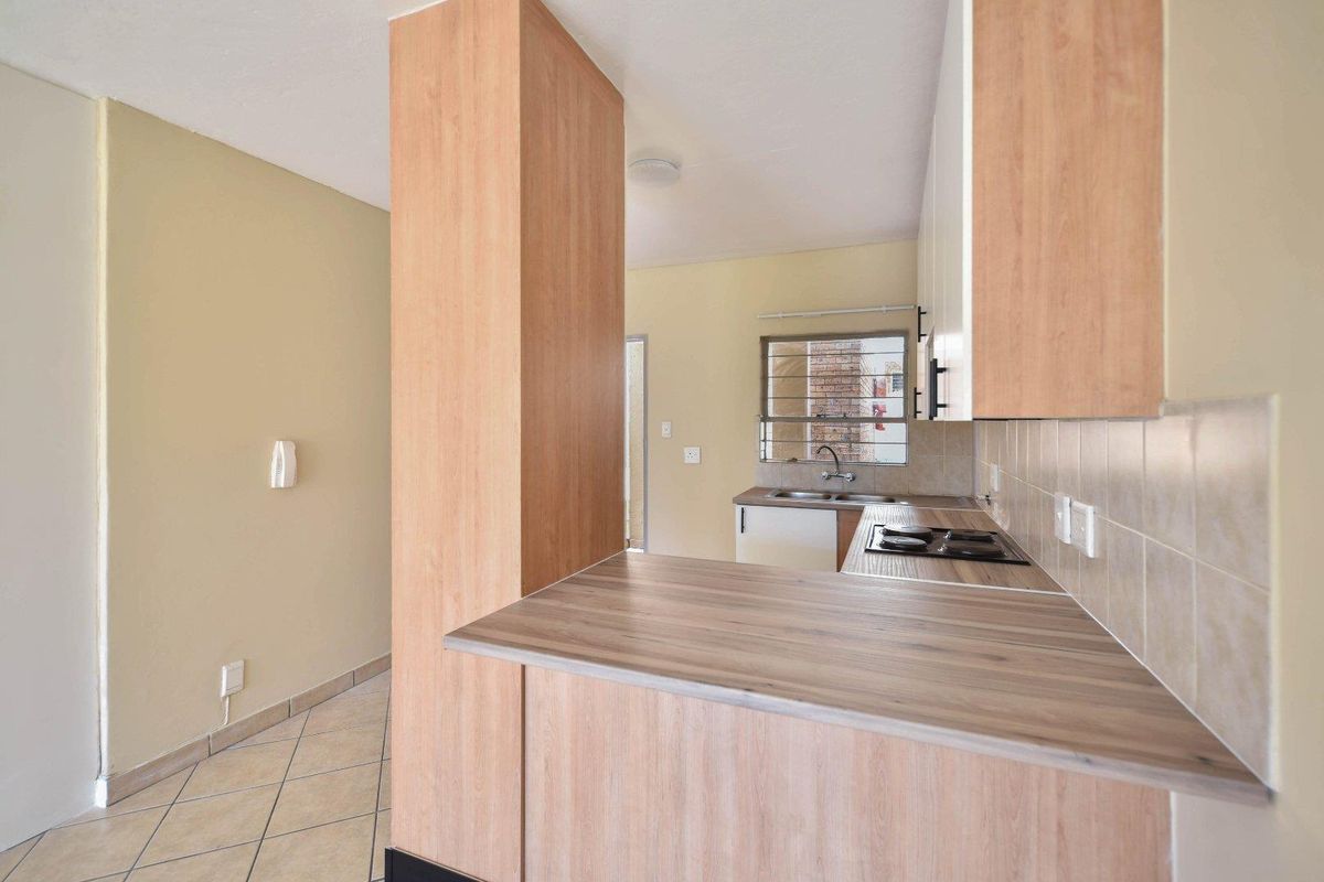 A functional kitchen featuring light wood-look cabinetry, laminate countertops, a built-in hob, and tiled flooring, offering a clean and practical workspace.