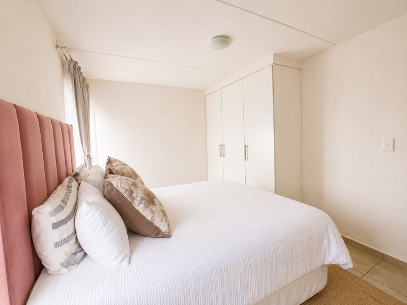 A bright bedroom featuring neutral walls, tiled flooring, and ample built-in cupboard storage.