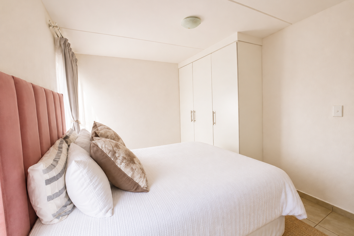 A bright bedroom featuring neutral walls, tiled flooring, and ample built-in cupboard storage.