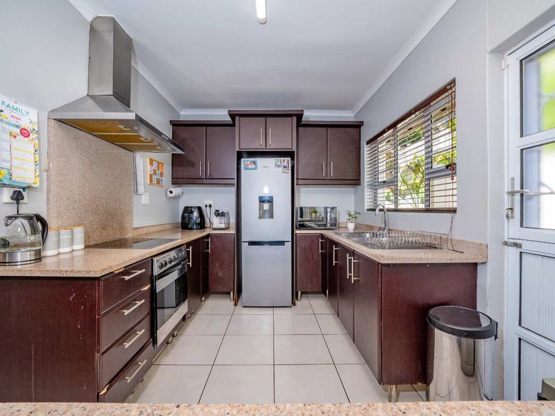 A functional galley-style kitchen featuring dark wood cabinetry, stone countertops, stainless steel appliances, and tiled flooring with direct access to the exterior.