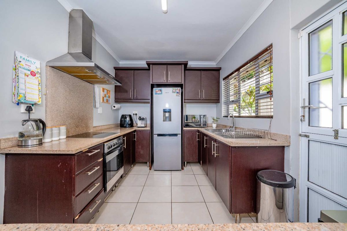 A functional galley-style kitchen featuring dark wood cabinetry, stone countertops, stainless steel appliances, and tiled flooring with direct access to the exterior.