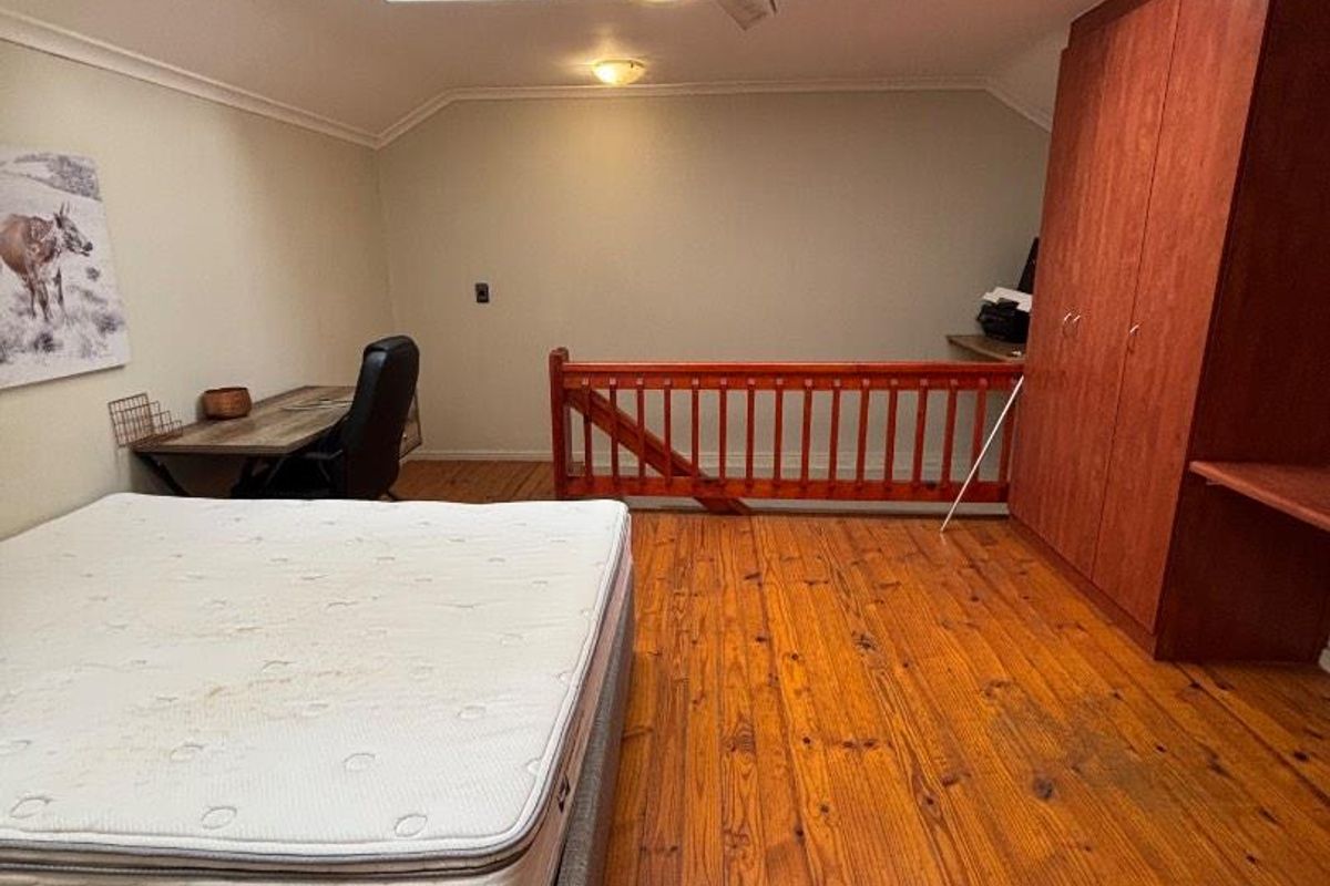 Spacious loft-style bedroom featuring polished timber flooring, a built-in wooden wardrobe, a ceiling fan, and a skylight providing natural light.