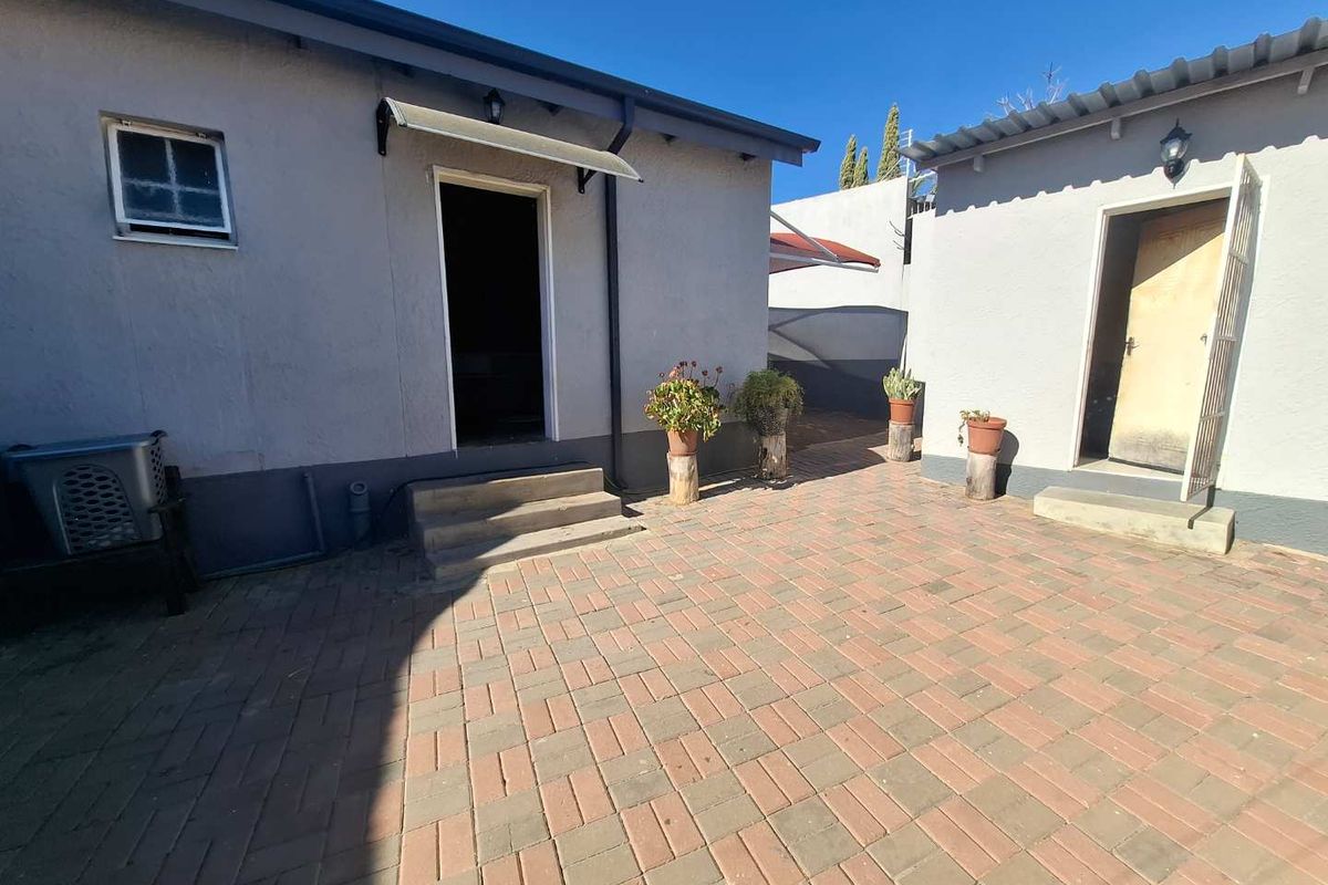 A paved rear courtyard area featuring access to two separate building entrances with exterior lighting fixtures.