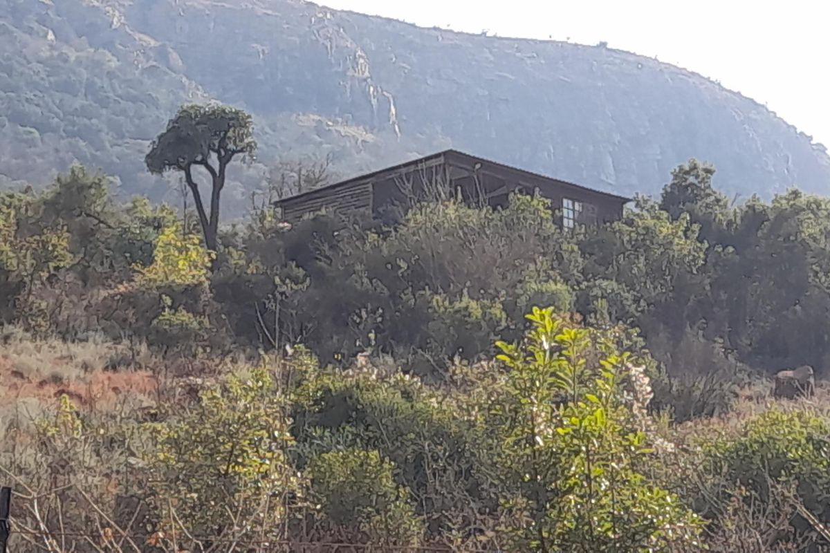 A distant view of a timber-clad structure nestled within a natural, bushveld landscape with mountain backdrop.