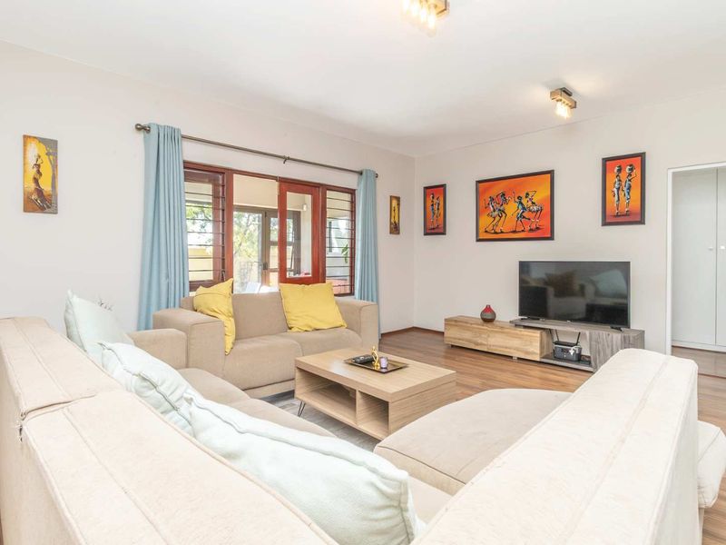 A well-maintained living room featuring laminate flooring, neutral walls, and timber-framed windows and doors providing natural light.