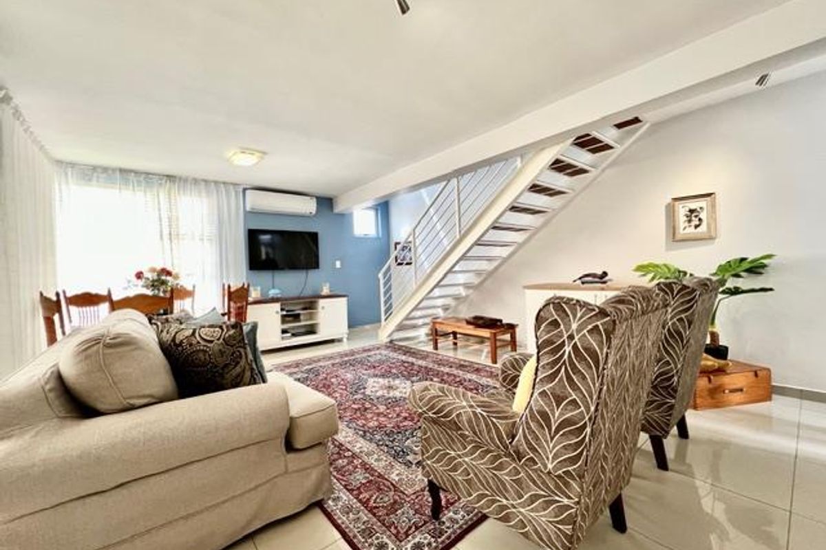 Spacious open-plan living area featuring tiled flooring, a split-system air conditioner, and a modern staircase with a metal balustrade.