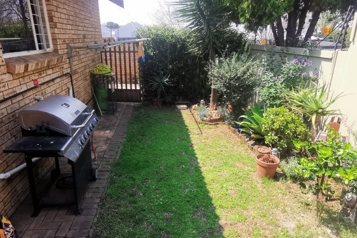 A private rear garden area featuring a brick exterior wall, paved walkway, and established landscaping with a boundary wall and security gate.