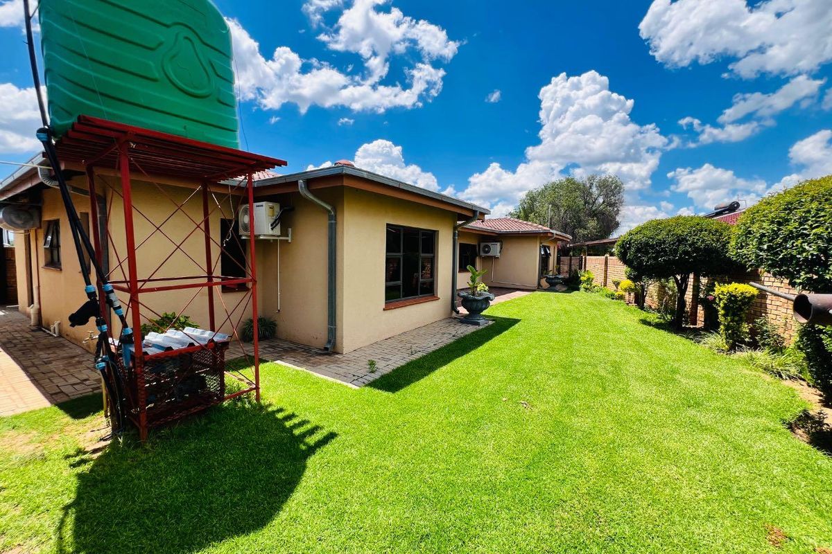 A well-maintained rear garden featuring a lush lawn, paved pathways, and a prominent elevated water storage tank.