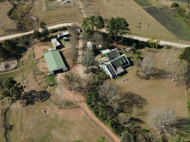 Aerial view of a farm property featuring a main farmhouse, large barn, outbuildings, and a dam set within expansive rural grounds.