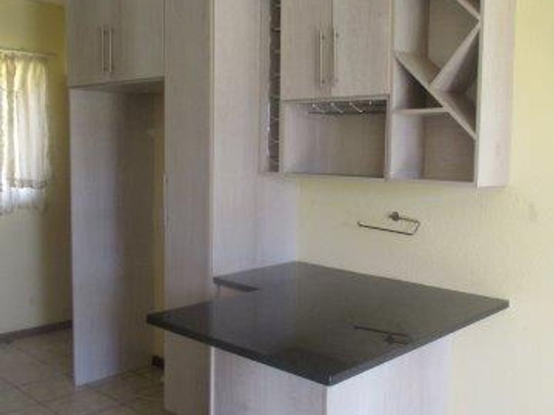 A functional kitchen area featuring light-toned built-in cabinetry, a dark granite breakfast bar, and tiled flooring.