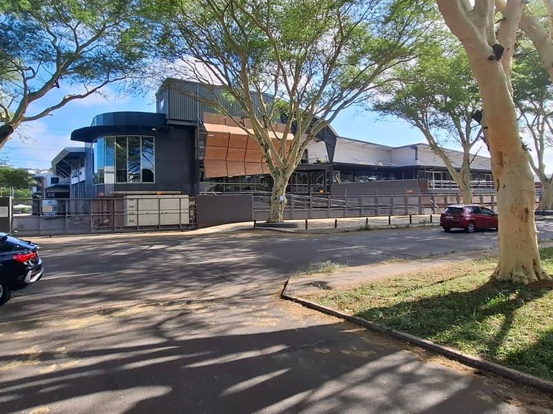 Exterior view of a modern commercial building featuring metal cladding, large glass windows, and secure perimeter fencing, situated in a landscaped setting.