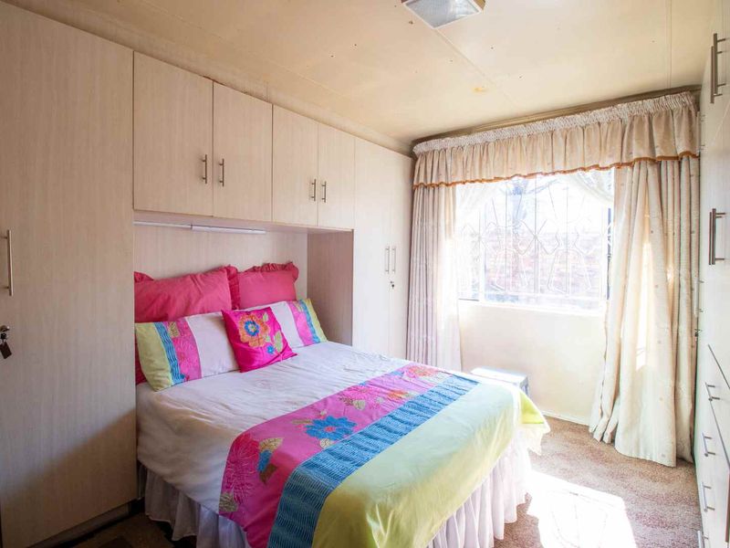 A bedroom featuring extensive built-in cupboard storage, carpeted flooring, and a window fitted with a security gate.