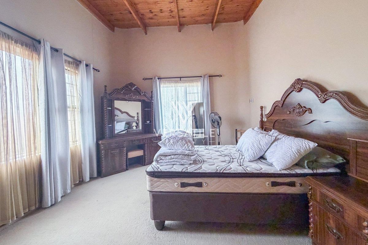 Spacious bedroom featuring high ceilings with exposed timber beams and neutral carpeting, offering a comfortable and well-lit living space.