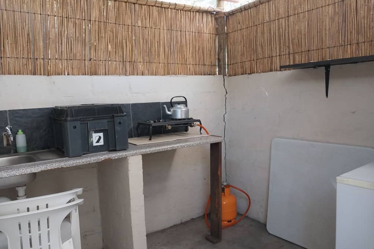 Outdoor kitchen area featuring a basic concrete countertop, sink, and gas cooking setup with reed screening and exposed masonry walls.