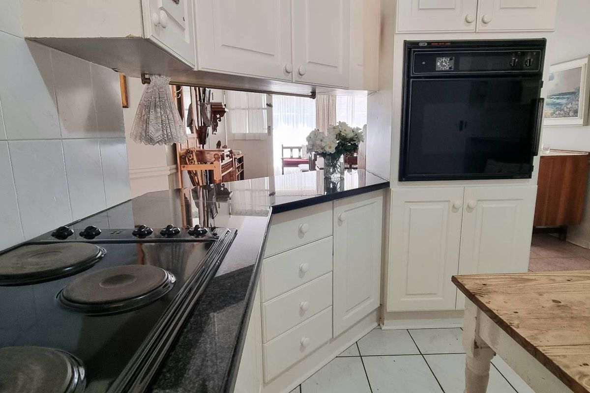 A functional kitchen featuring white cabinetry, a black granite countertop, a built-in oven, and a black electric hob with tiled splashbacks.