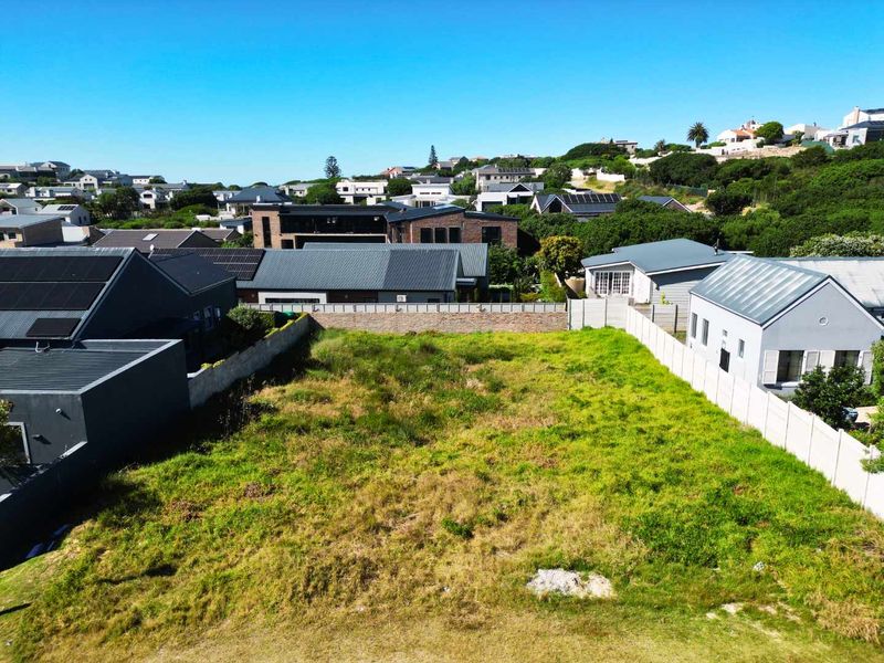 An aerial view of a vacant residential plot situated within an established suburban neighborhood, featuring boundary walls and surrounding residential properties.